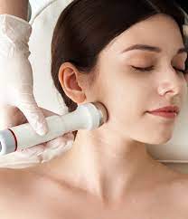 Woman using a handheld electronic device on her face, with a focus on skincare.