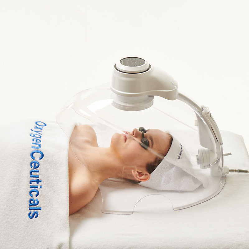 Woman receiving a facial treatment with 'Oxygen Ceuticals' equipment on a white background