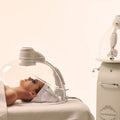 Woman receiving a facial treatment with a machine labeled 'AstridoneFacial' on a white background