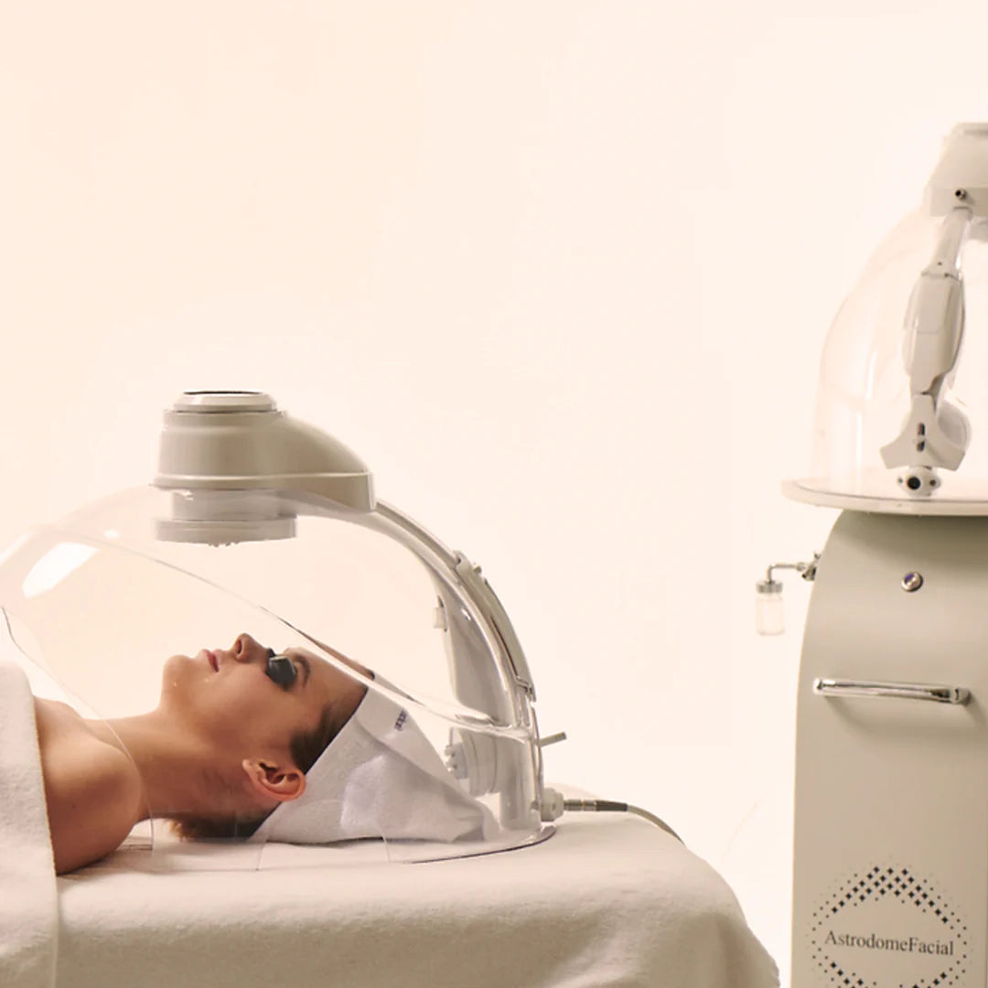Woman receiving a facial treatment with a machine labeled 'AstridoneFacial' on a white background