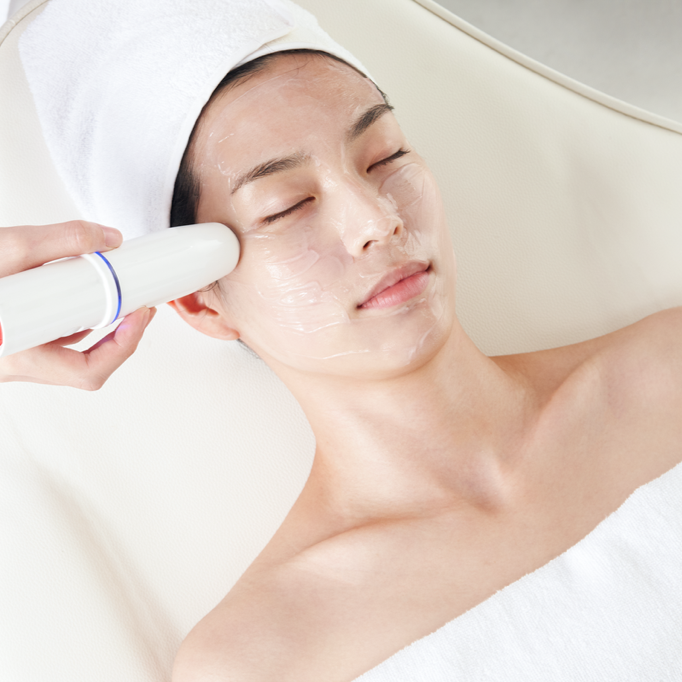 Person receiving a facial treatment with a handheld device on a white background