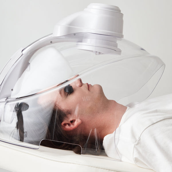 Person receiving a hair treatment under a large white hood with a reflective surface.