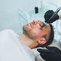 Person receiving a facial treatment with a device from a professional in a clinical setting.