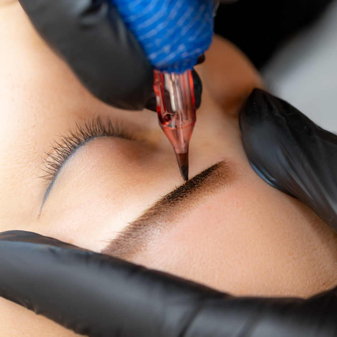 A close-up image of a person receiving a brow tattoo treatment, with a focus on the tattooing needle and the developing shape of the eyebrow.