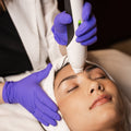 Person receiving a facial treatment with a device held by a professional wearing gloves.