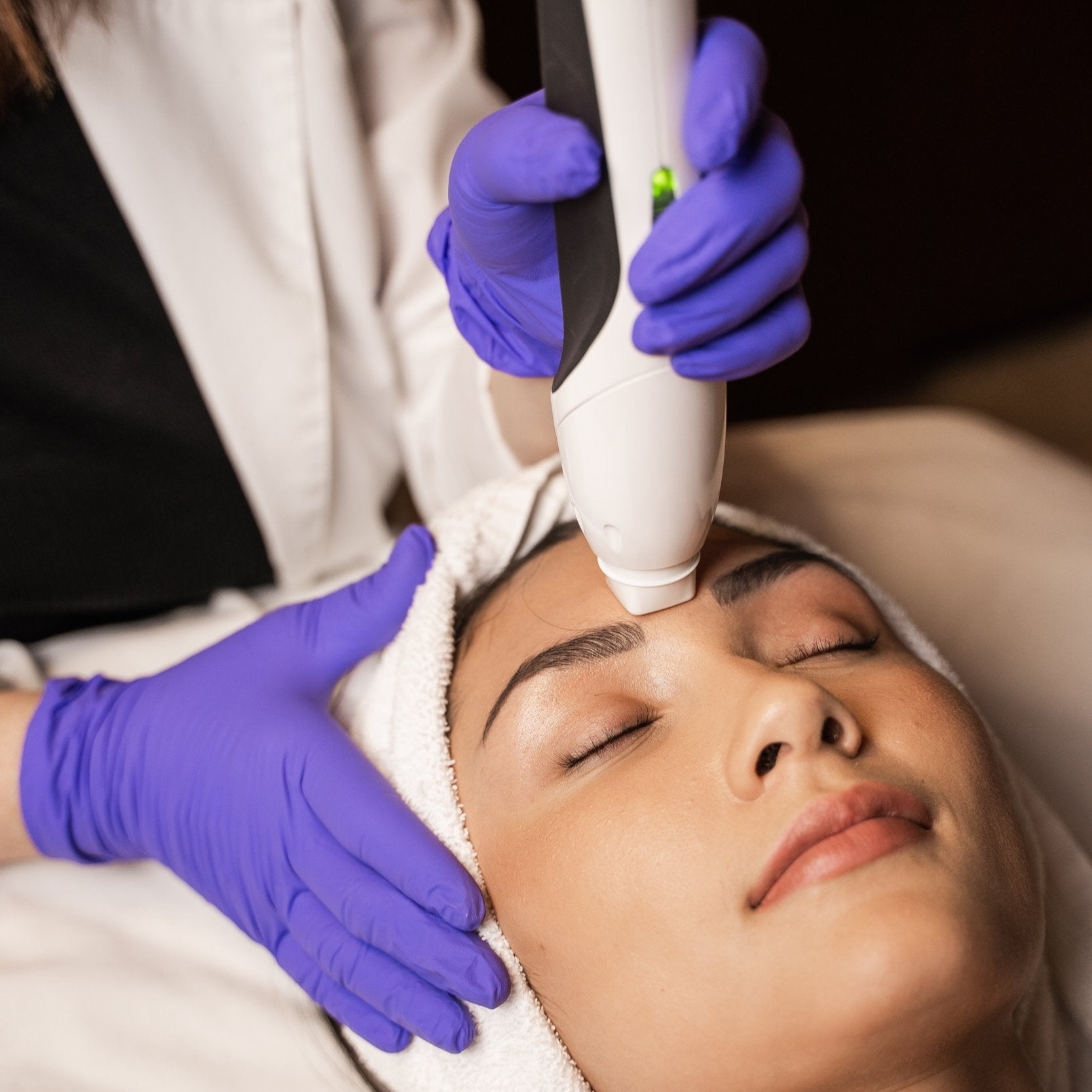 Person receiving a facial treatment with a device held by a professional wearing gloves.