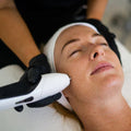 Woman receiving a facial treatment with a device held by a professional.