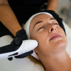 Woman receiving a facial treatment with a device held by a professional.